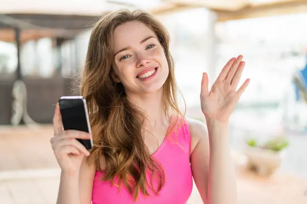 Ung Rödhårig Kvinna Som Använder Mobiltelefon Utomhus Saluterar Med Handen — Stockfoto