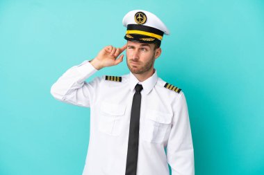 Kafkasyalı uçak pilotu mavi arka planda izole edilmiş. Şüpheleri var ve kafası karışmış bir yüz ifadesi var.