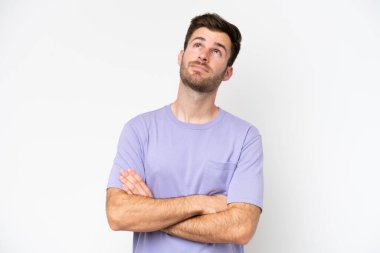 Beyaz arka planda izole edilmiş genç beyaz adam gülümserken yukarı bakıyor.