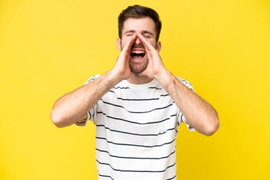Genç beyaz adam sarı arka planda izole edilmiş bağırıyor ve bir şey duyuruyor.