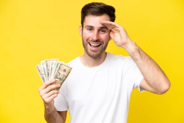 Kafkasyalı genç bir adam, sarı arka planda, sürpriz bir ifadeyle izole edilmiş bir sürü para alıyor.