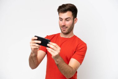 Beyaz arka planda izole edilmiş genç beyaz adam cep telefonuyla oynuyor.