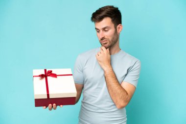 Young caucasian man holding a gift isolated on blue background with sad expression