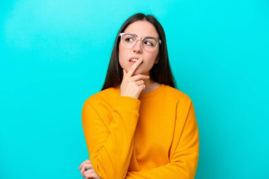 Mavi arka planda gözlüklü ve kuşkuları olan genç bir kız.