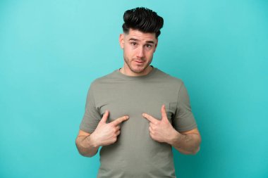 Mavi arka planda izole edilmiş genç beyaz adam kendini işaret ediyor.