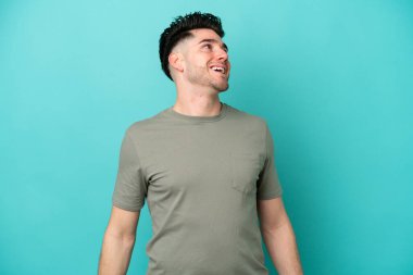 Kafkasyalı genç adam mavi arka planda tek başına gülüyor.