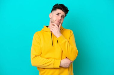 Kafkasyalı genç adam mavi arka planda izole edilmiş bir şekilde yukarı bakarken bir fikir düşünüyor.