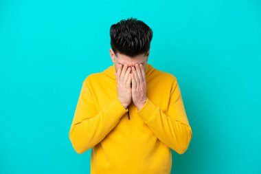 Kafkasyalı genç adam mavi arka planda izole edilmiş, yorgun ve hasta bir ifadeyle.