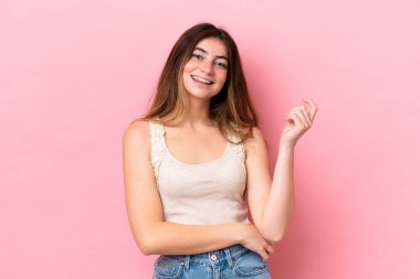 Pembe arka planda izole edilmiş genç beyaz kadın gülüyor.