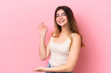 Pembe arka planda izole edilmiş genç beyaz kadın, davet edilmek için ellerini yana uzatıyor.