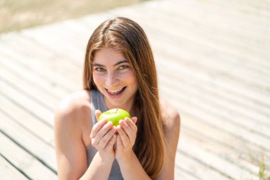 Genç, güzel, beyaz bir kadın elinde mutlu bir ifadeyle bir elma tutuyor.