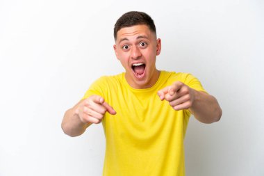 Beyaz arka planda izole edilmiş genç Brezilyalı adam şaşırmış ve ön tarafı işaret ediyor.