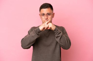 Pembe arka planda izole edilmiş genç Brezilyalı bir adam sessizlik işareti gösteriyor.