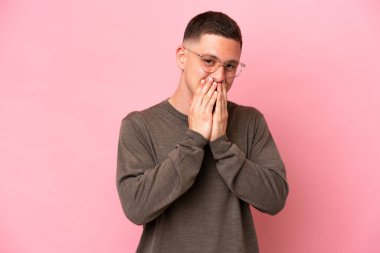 Pembe arka planda izole edilmiş genç Brezilyalı adam mutlu ve gülümseyen elleriyle ağzını kapatıyor.