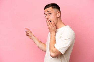 Pembe arka planda izole edilmiş genç Brezilyalı bir adam sürpriz bir ifadeyle işaret ederken...