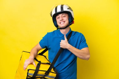 Young Brazilian man with thermal backpack isolated on yellow background giving a thumbs up gesture