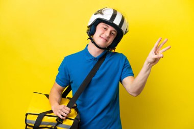 Sırt çantalı genç Brezilyalı adam sarı arka planda izole edilmiş mutlu ve parmaklarıyla üçe kadar sayıyor.