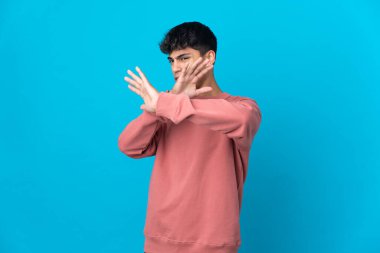 İzole edilmiş mavi arka planda genç bir adam gergin ellerini öne uzatıyor.