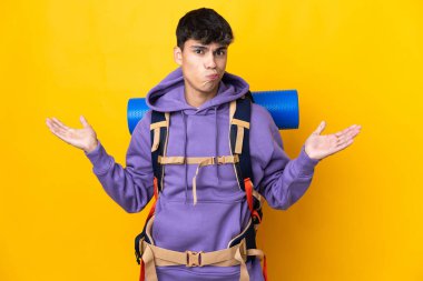 Sarı arka plan üzerinde büyük bir sırt çantası olan genç dağcı el kaldırırken kuşkuları var.