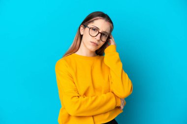 Kafkasyalı genç bir kadın mavi arka planda izole edilmiş. Şüpheleri var.