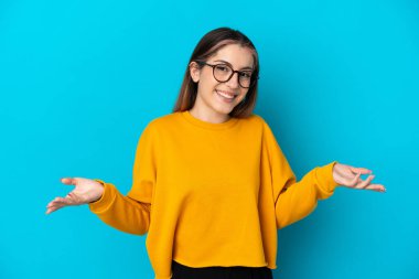 Mavi arka planda izole edilmiş genç beyaz kadın mutlu ve gülümsüyor.