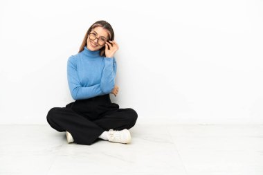 Genç beyaz kadın yerde oturuyor, gözlüklü ve mutlu.