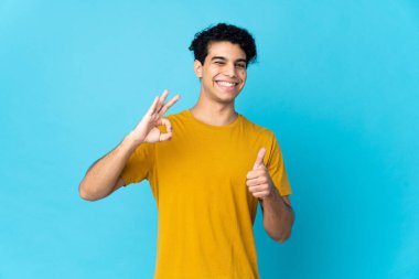 Genç Venezuelalı bir adam mavi arka planda izole edilmiş.