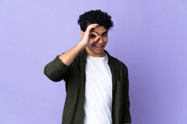 Genç Venezuelalı adam mor arka planda izole edilmiş. Parmaklarıyla işaret veriyor.
