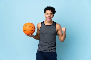 Genç Venezuelalı adam mavi arka planda izole edilmiş basketbol oynuyor.