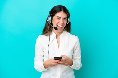 Tele pazarlamacı, mavi arka planda izole edilmiş kulaklıkla çalışan İtalyan kadın şaşırdı ve bir mesaj gönderiyor.