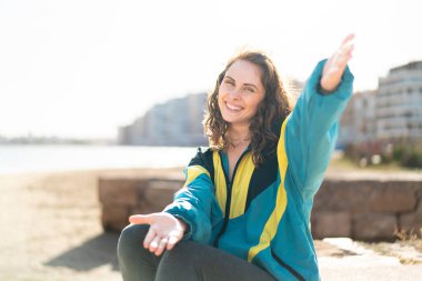 Açık havada genç bir kadın sunuyor ve davet ediyor.