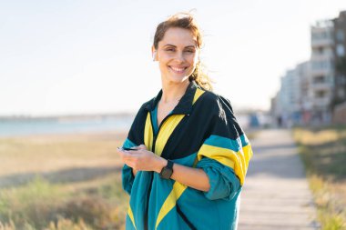 Açık havada giyinen ve telefonlu müzik dinleyen genç bir kadın.