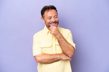 Mor arka planda izole edilmiş orta yaşlı beyaz bir adam yana bakıyor ve gülümsüyor.