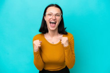 Mavi arka planda izole edilmiş genç beyaz kadın galibiyeti kutluyor.