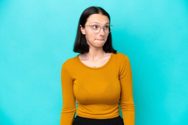 Kafkasyalı genç bir kadın mavi arka planda izole edilmiş, yukarı bakarken şüpheleri var.