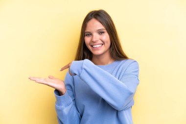 Sarı arka planda izole edilmiş genç beyaz kadın bir ilan vermek için avucunun içinde hayali bir mekan tutuyor.