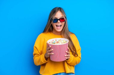 Mavi arka planda 3 boyutlu gözlüklü ve elinde koca bir kova patlamış mısır tutan beyaz bir kadın.