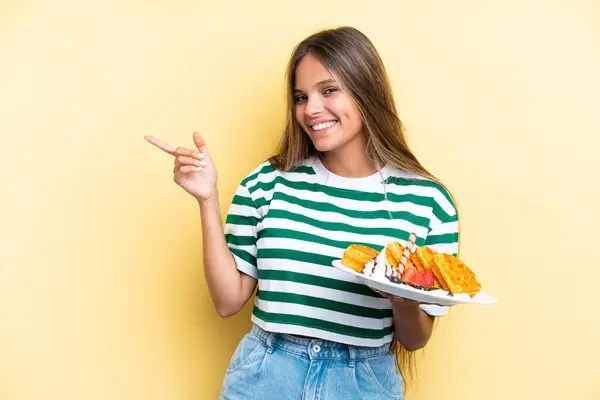 Young Caucasian Woman Holding Waffles Isolated Yellow Background Pointing Finger — Stock Photo, Image