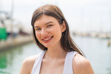 Genç, güzel bir kadın açık havada, mutlu bir ifadeyle.