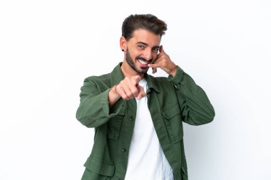 Beyaz arka planda izole edilmiş genç beyaz bir adam telefon jesti yapıyor ve ön tarafı işaret ediyor.