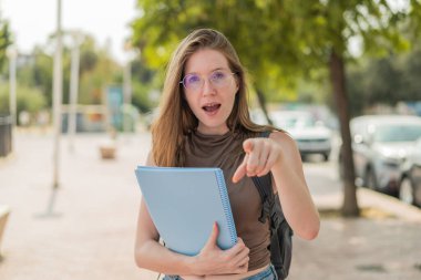 Açık havada gözlüklü Fransız öğrenci şaşırmış ve ön tarafı işaret ediyor.