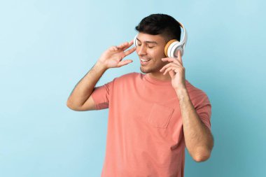 Genç Kolombiyalı adam mavi arka planda izole edilmiş müzik dinliyor ve şarkı söylüyor.