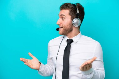 Telemarketer caucasian man working with a headset isolated on blue background with surprise facial expression