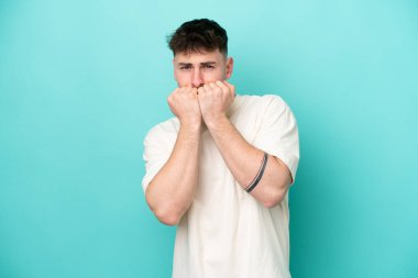 Genç, beyaz, yakışıklı bir adam mavi arka planda izole edilmiş. Gergin ve korkmuş.