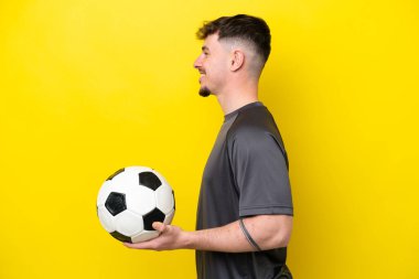 Genç futbolcu sarı arka planda izole edilmiş. Yan pozisyonda gülüyor.