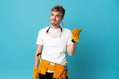 Genç elektrikçi, yalıtılmış duvarın üzerinden bir ürün sunmak için yan tarafı işaret ediyor.