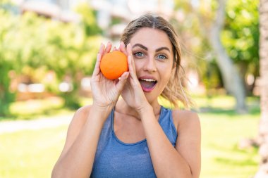 Açık havada elinde portakal tutan genç sarışın kadın.
