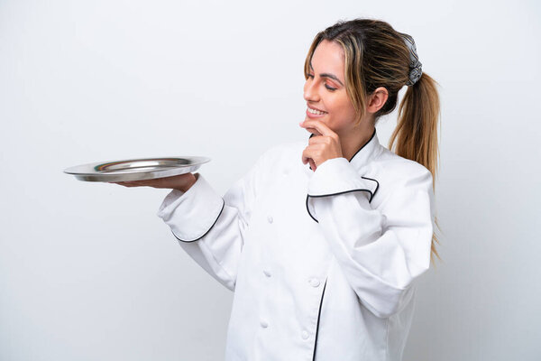 Young chef woman with tray isolated on white background looking to the side and smiling