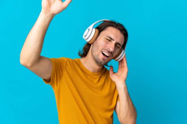 Genç yakışıklı adam mavi arka planda izole edilmiş müzik ve dans dinliyor.