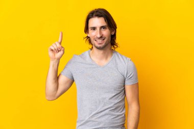 Sarı arka planda izole edilmiş genç yakışıklı adam harika bir fikre işaret ediyor.